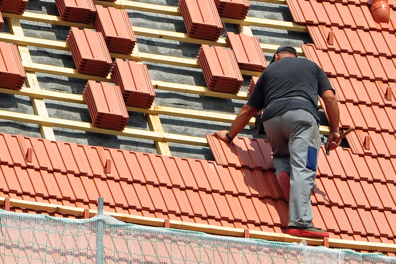 Elm Bau - Dachdecker auf einem Dach beim Dachziegel verlegen